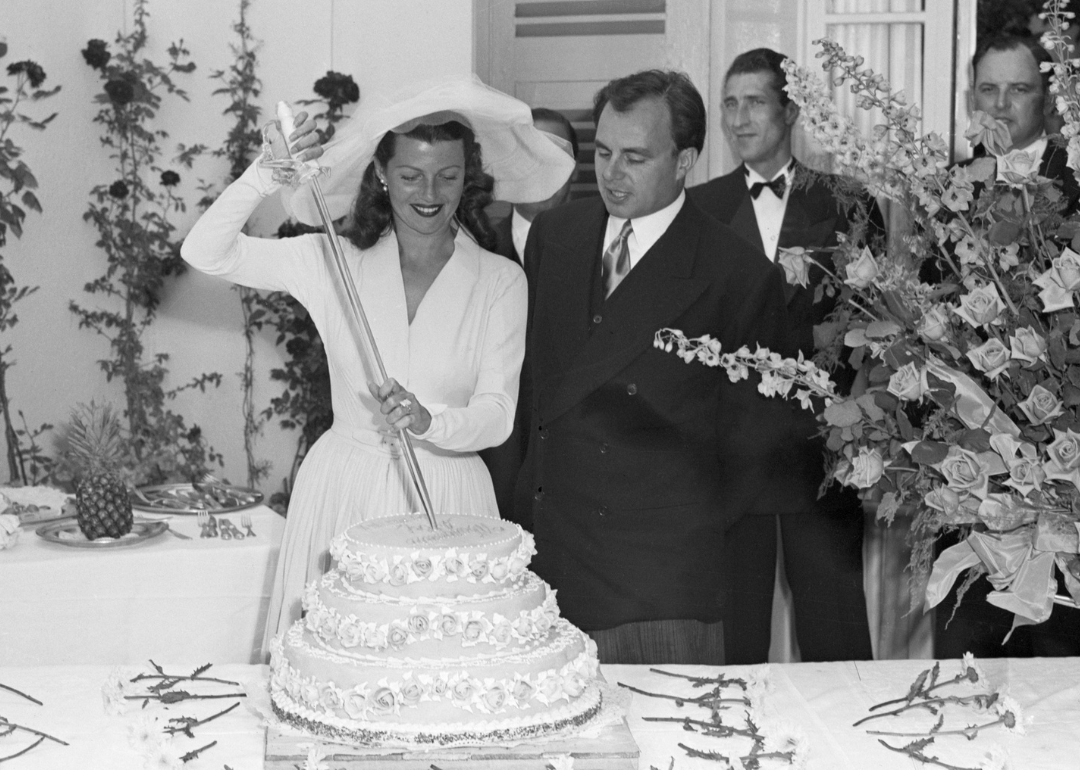 Rita Hayworth, with her husband, Prince Aly Khan, cuts their wedding cake with a sword.