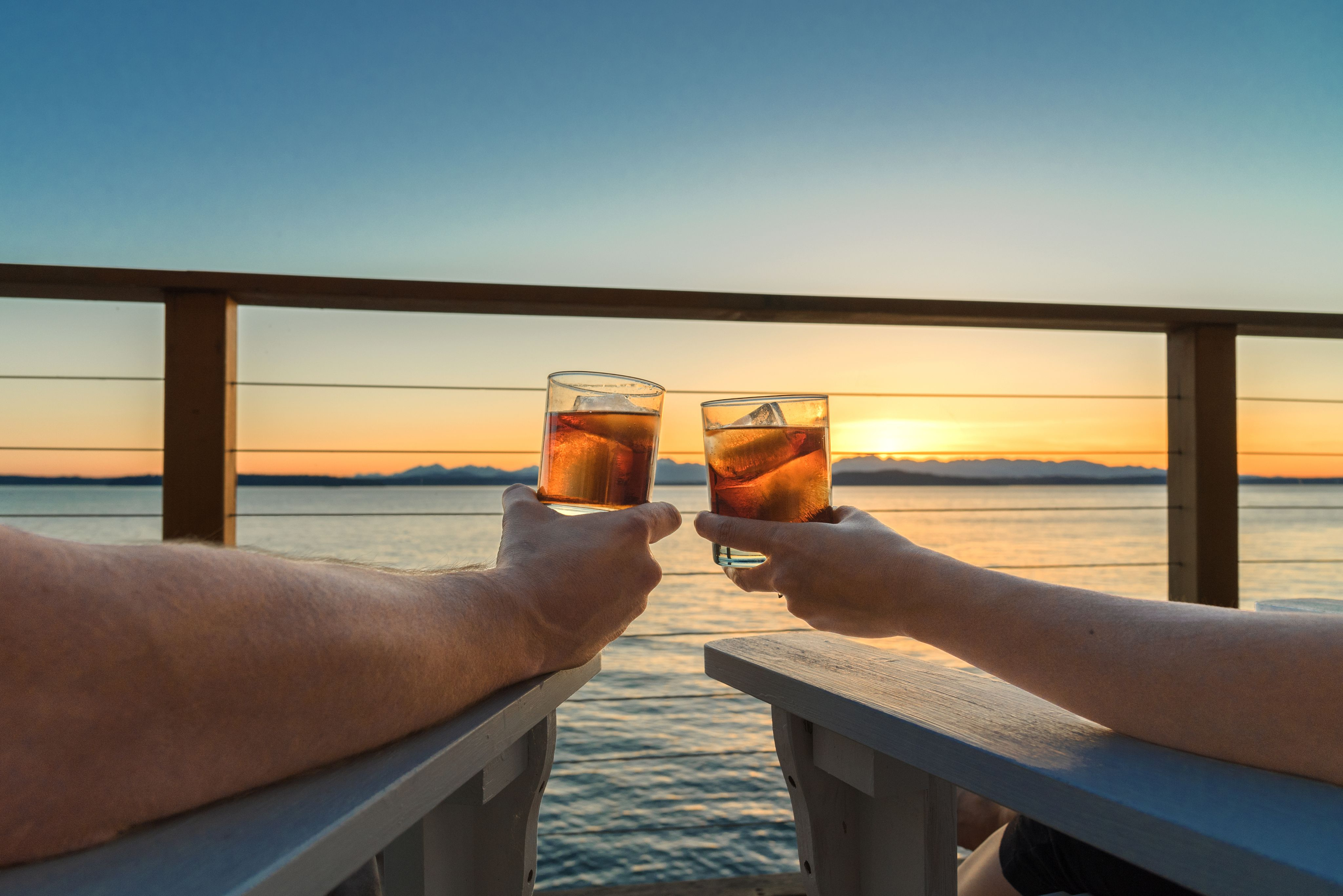 Beautiful sunset view from the deck, couple holding up glasses to toast.