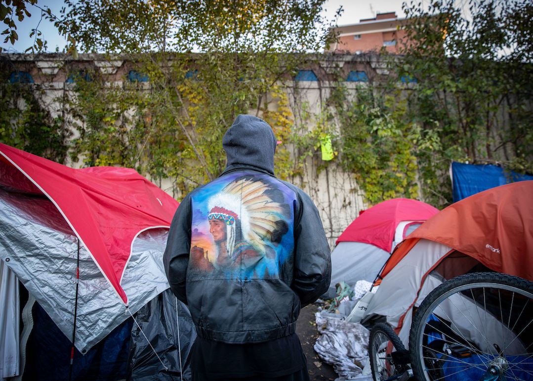 Person photographed from behind standing in front of tents at homeless encampment in Minneapolis, Minnesota.