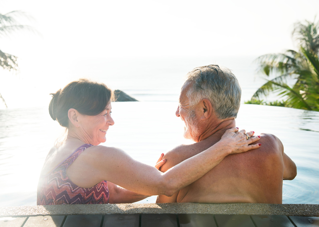 Retired couple relaxing in a pool surrounded by palm trees.