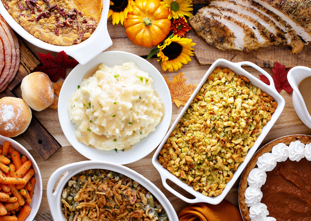 Dishes of mashed potatoes, candied yams, carrots, stuffing, and green bean casserole fill a Thanksgiving dining table.