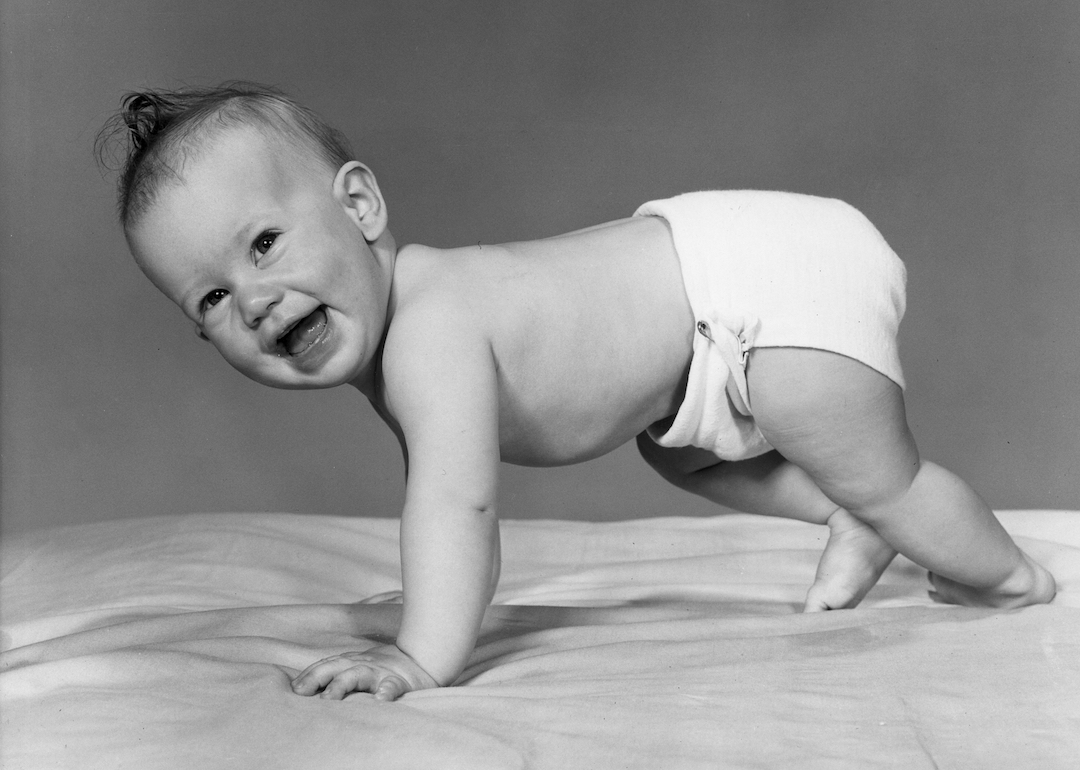 A baby smiles while crawling on all fours, wearing a diaper, in the 1940s.