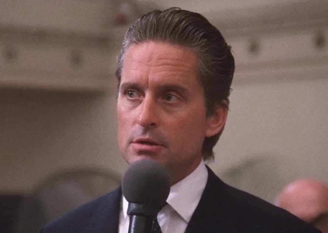 Michael Douglas stands at a microphone as Gordon Gekko in the 1987 movie 'Wall Street,' giving his famous 'greed is good' speech.