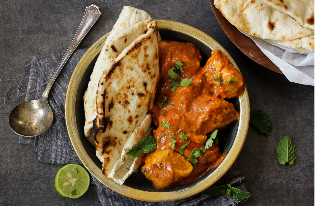 Butter chicken with naan bread on a plate next to a lime.
