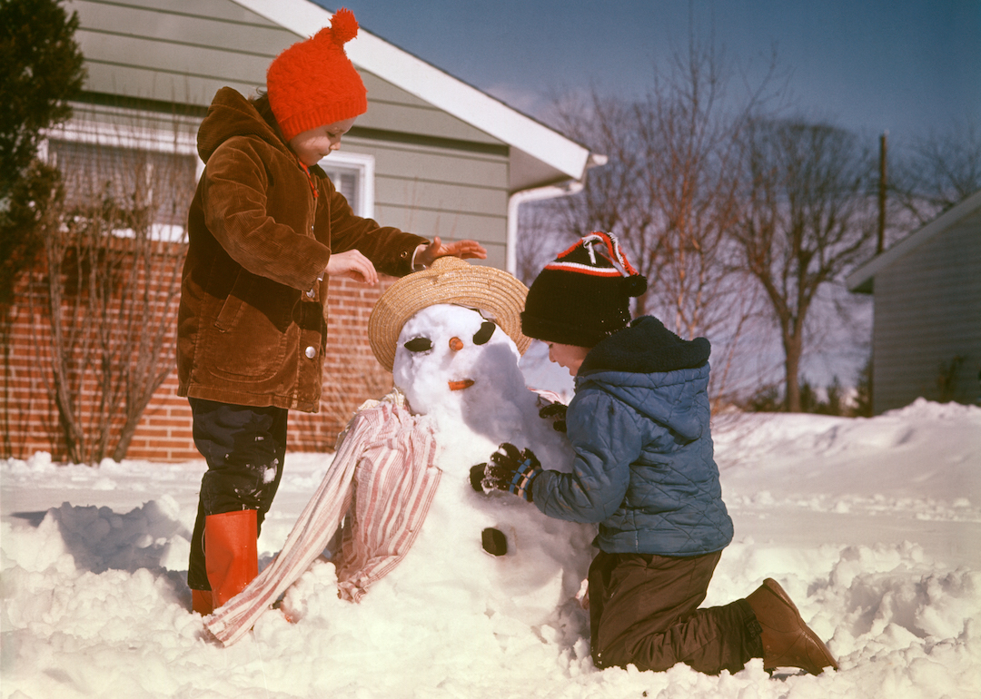 Siblings build a snow person in front of their suburban home in the 1970s.