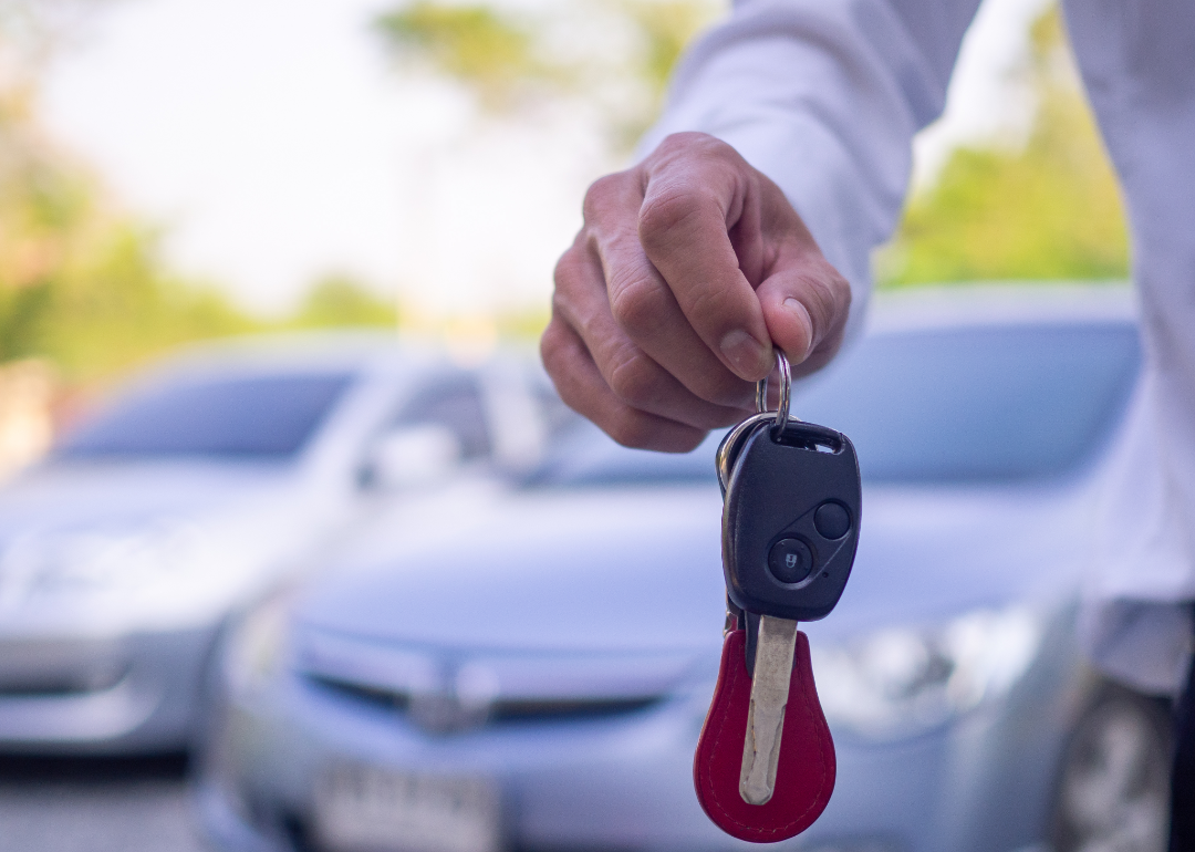 Closeup of car salesperson holding car keys while standing in front of cars.