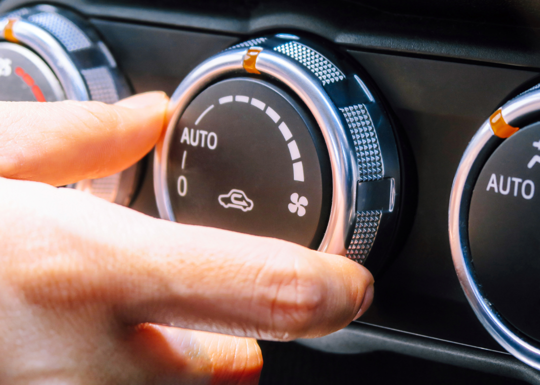 A hand adjusts the AC settings in a car.