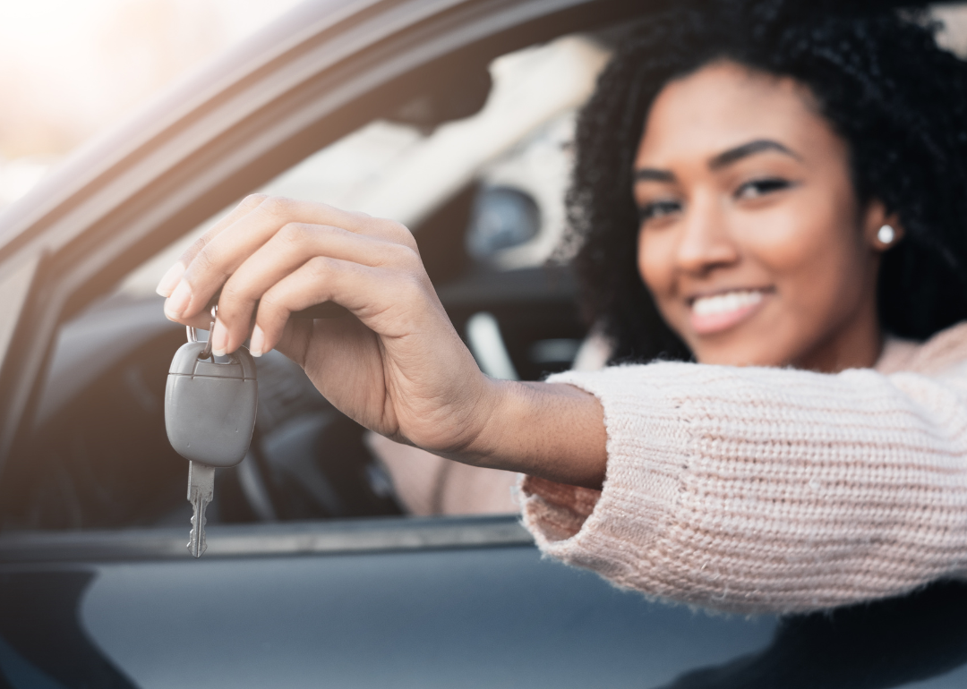Woman holding up car key while inside car.