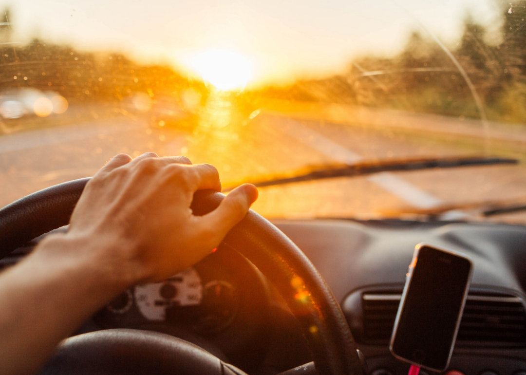 A hand operates a steering wheel in a car with the sun streaming in.