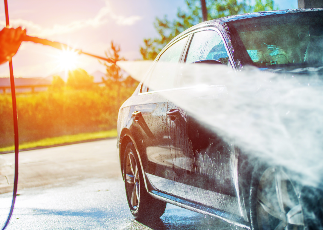 Water sprays from a hose onto a car in the hot sun.