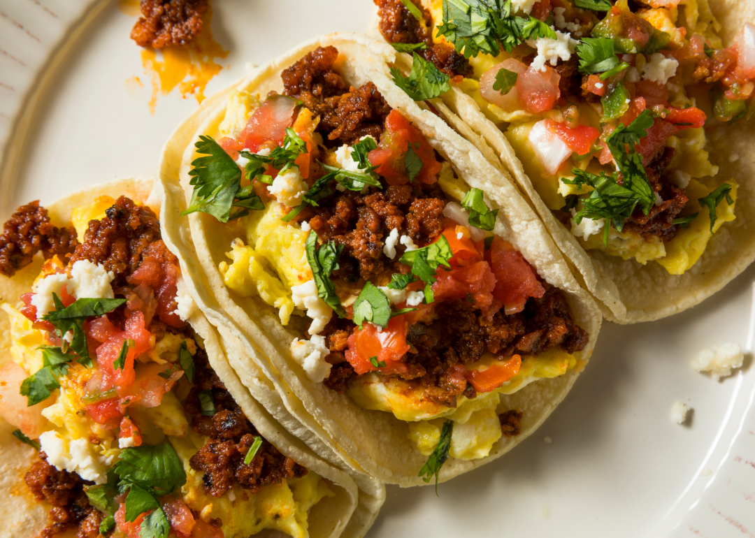 Three breakfast tacos filled with chorizo, egg, tomatoes, and cilantro on a white plate.