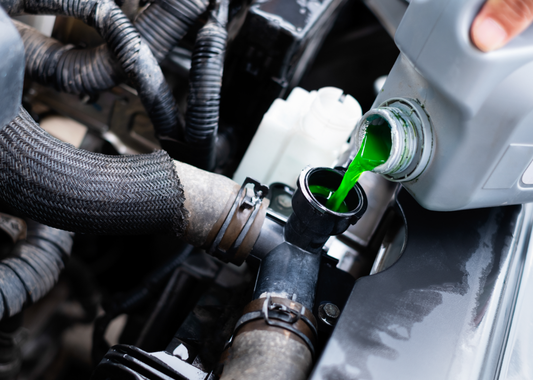 Green automobile coolant is poured from a grey container.