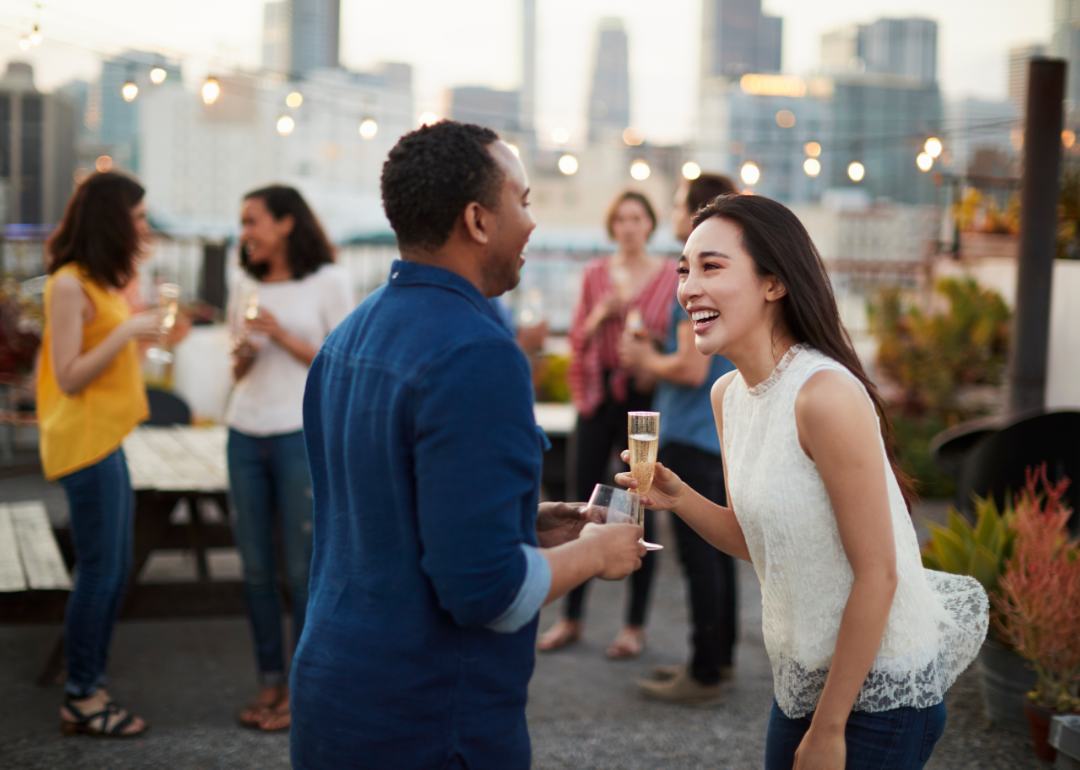 Friends laughing and talking at a rooftop bar in a city at sunset.