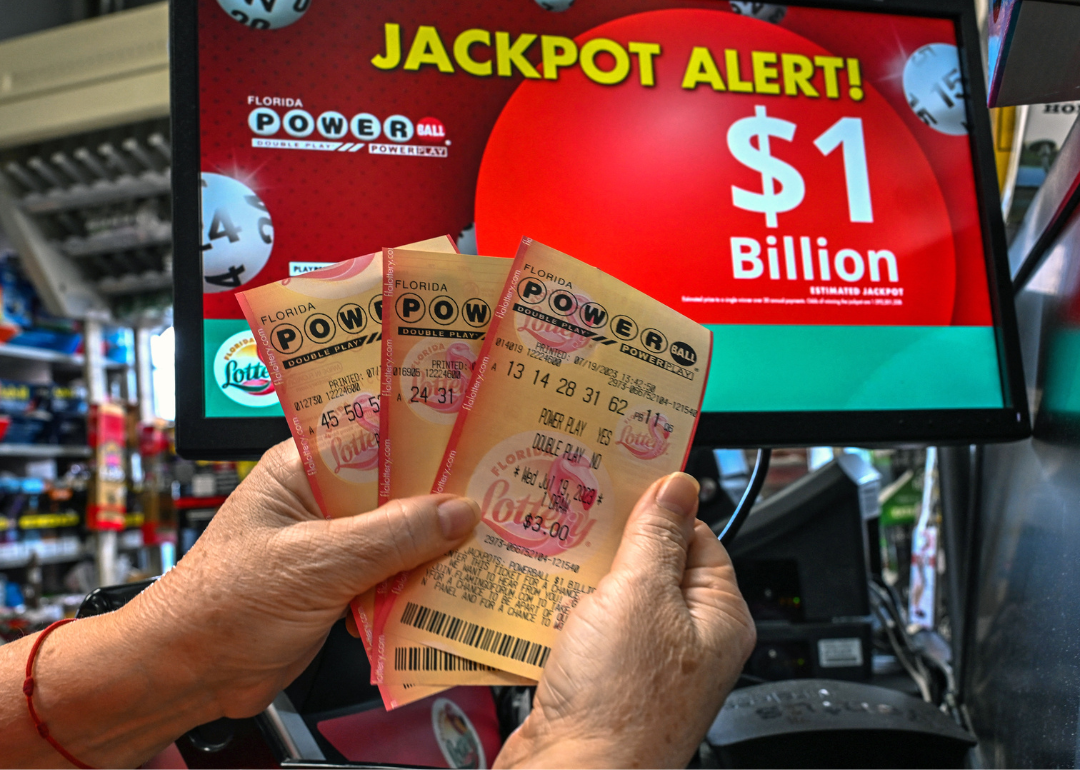 A person holds Powerball tickets in front of a sign announcing a billion dollar jackpot.