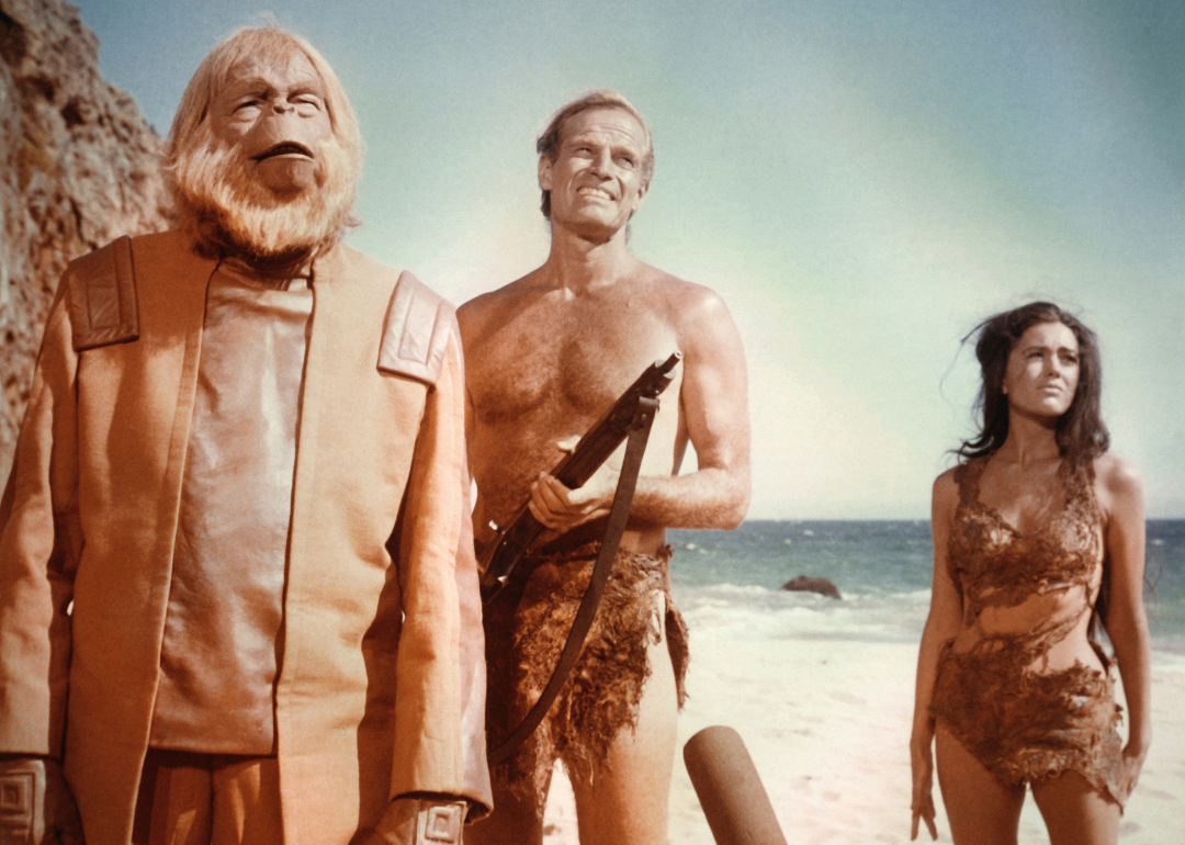 Actor Charlton Heston holding rifle with along with actors Linda Harrison and Maurice Evans on a beach in a scene from the 1968 film "Planet of the Apes"