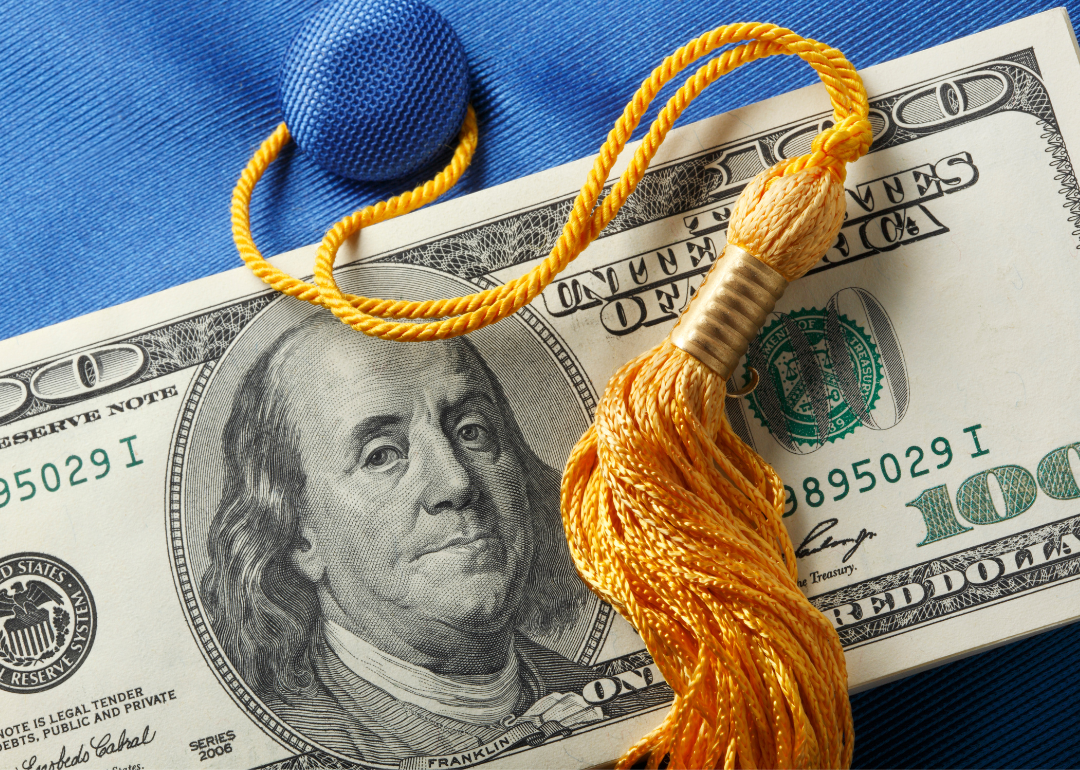 Money laying on top of blue graduation cap with yellow tassel.