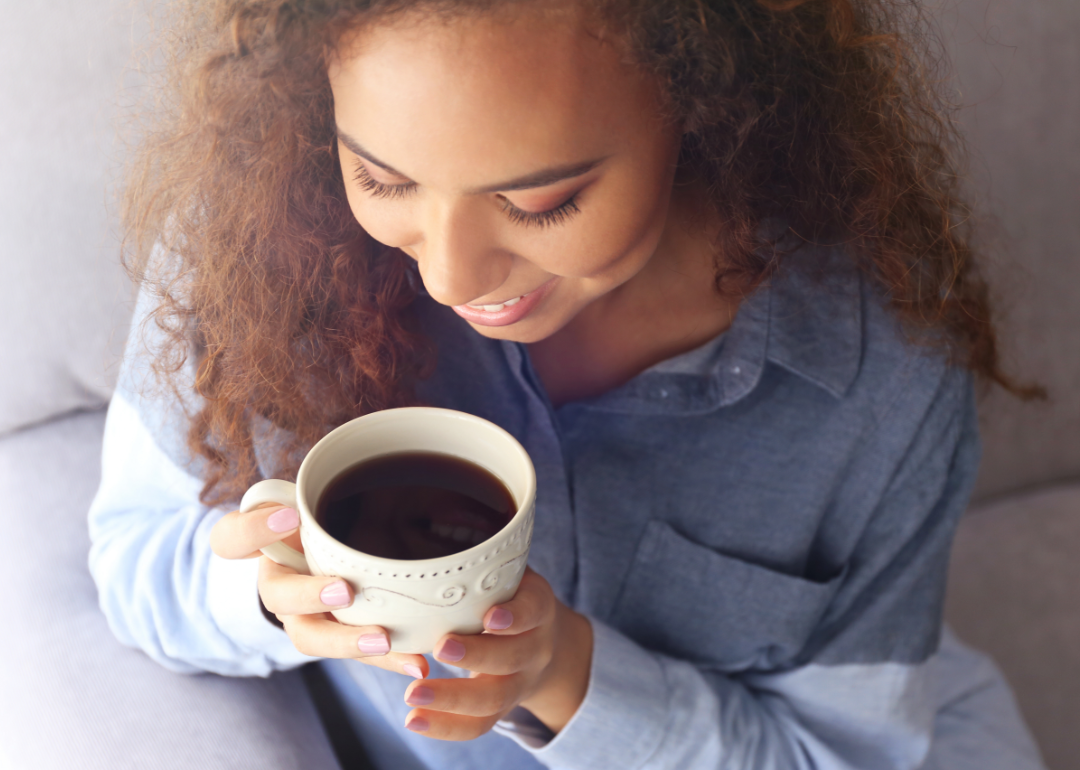 A woman on a couch holds a cup of coffee.