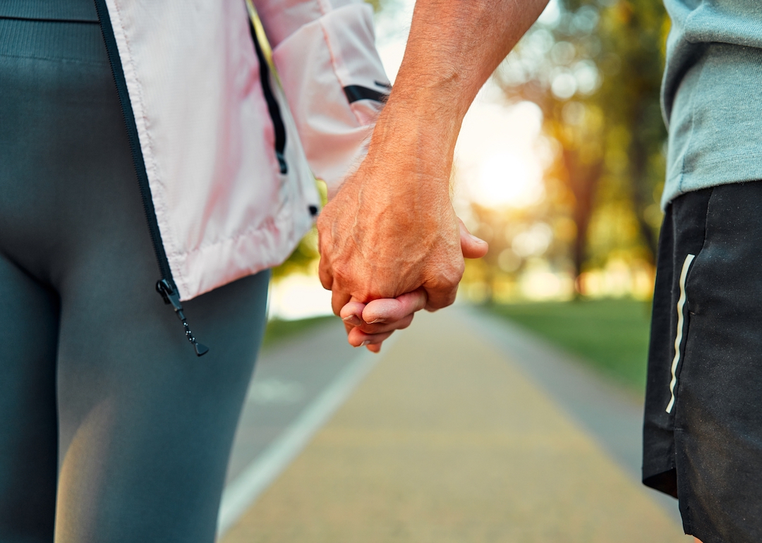 Close-up of the hands of an older couple holding hands while walking in the park outdoors.