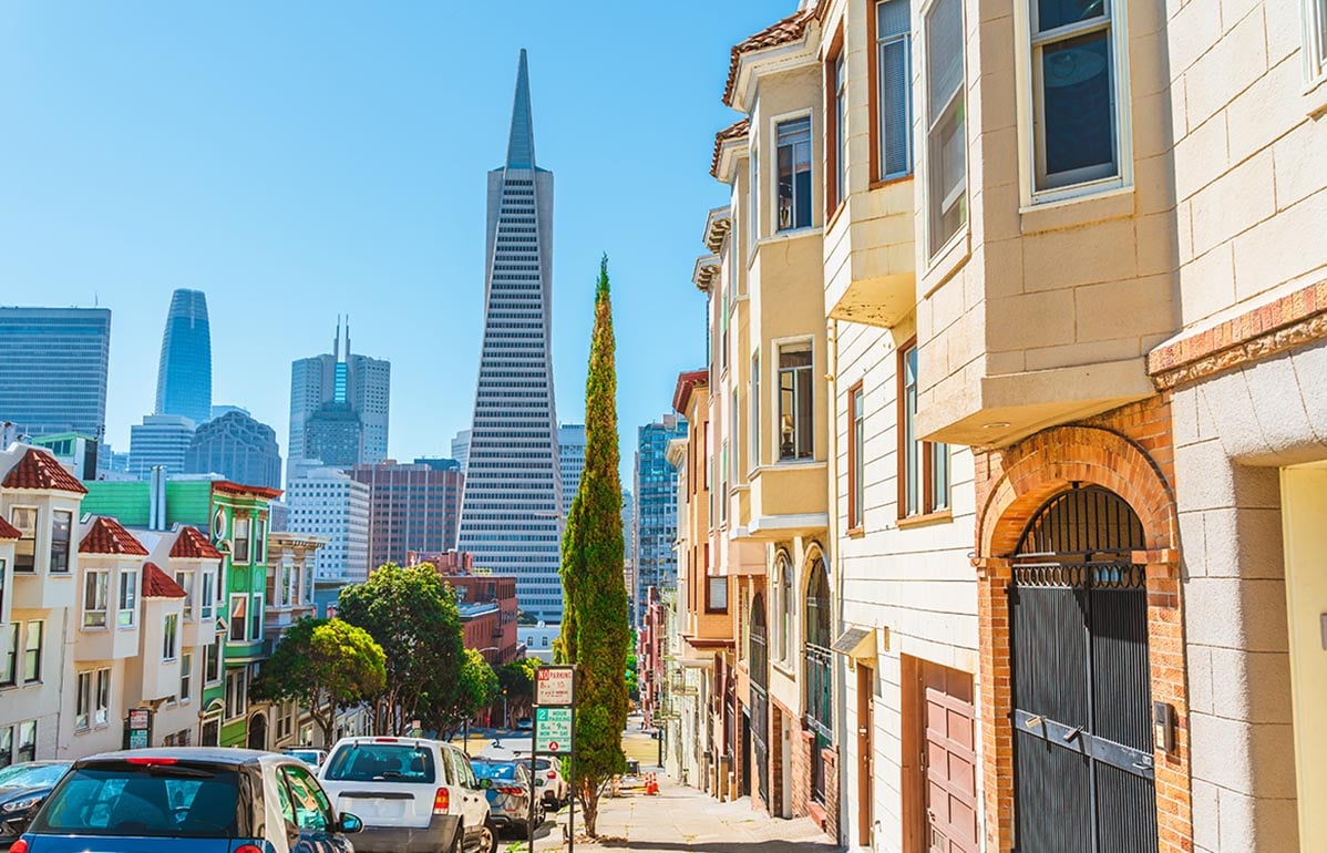 San Francisco street lined with homes and a view of the Transamerica Tower.