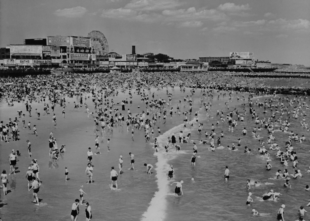 Elevated view along the coastline showing a crowded beach and ocean in Coney Island, New York, circa 1963.