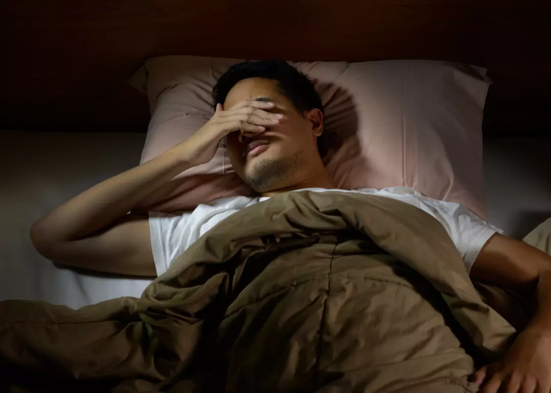 Person lying in bed in the dark with a hand over their eyes