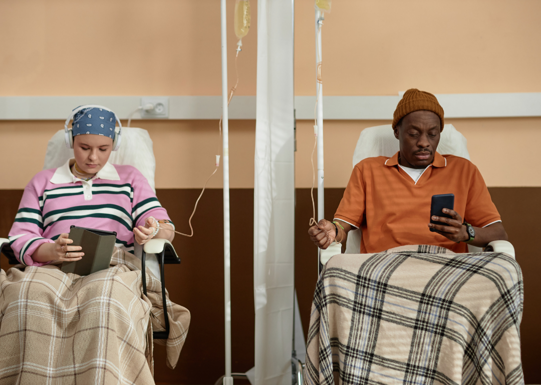 Two people sitting side-by-side and scrolling on their phones while getting chemotherapy treatment in clinic