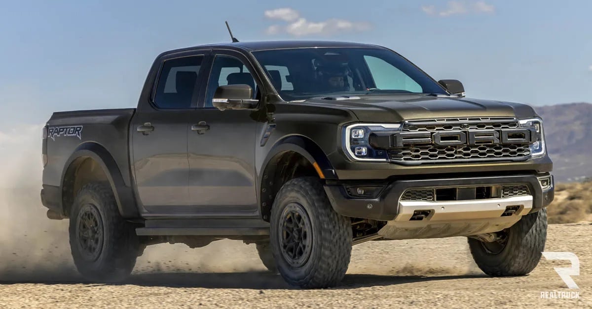 A black Ford Ranger Raptor driven in a sandy wide lot.