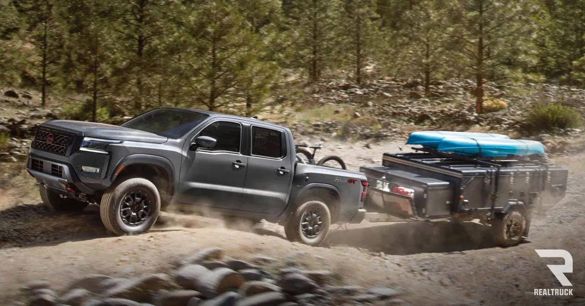 A black Nissan Frontier towing a kayak trailer on a rocky road.
