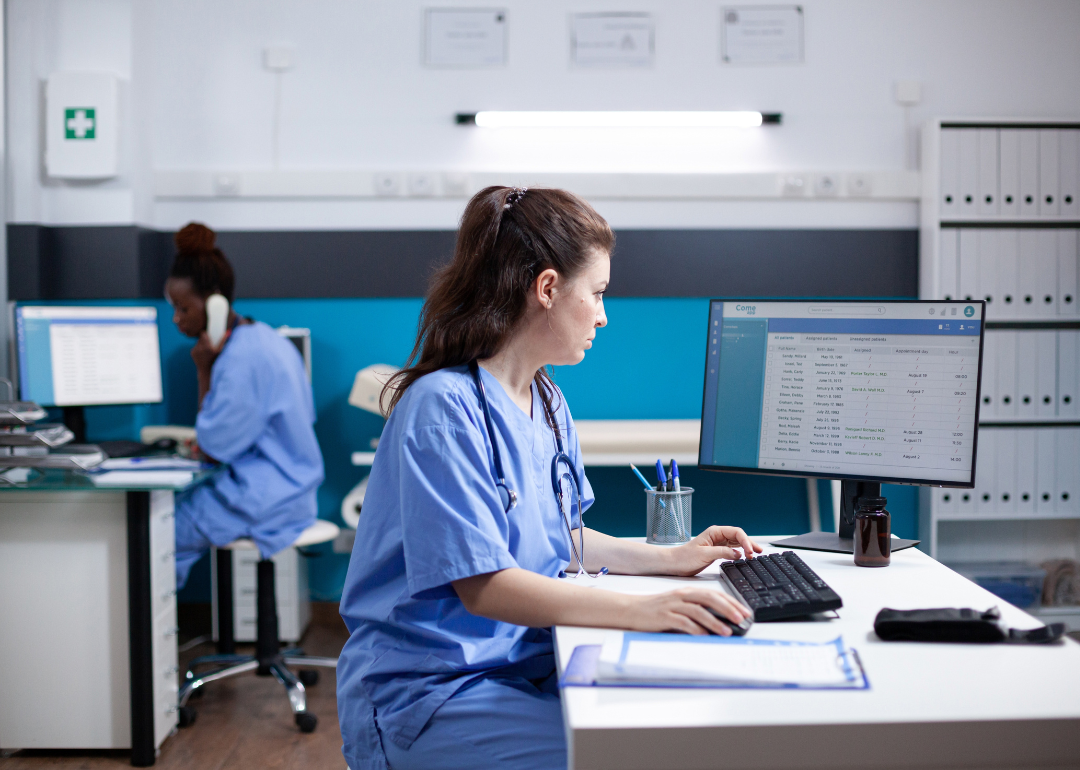 Nurse practitioners in scrubs filling out patient details on computers in a medical clinic