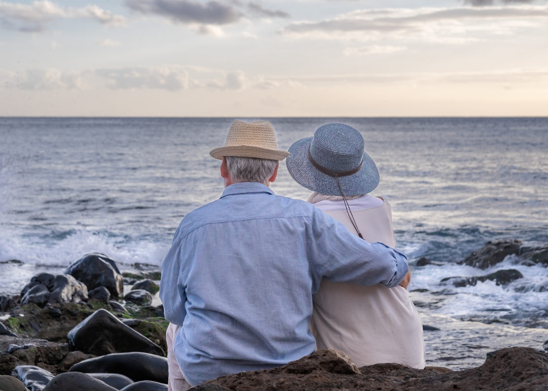 Elderly couple sitting on a rocky beach and looking at the horizon