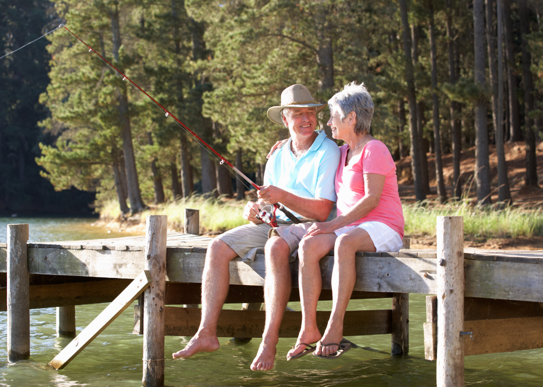Senior couple sitting on a lakeside dock and fishing