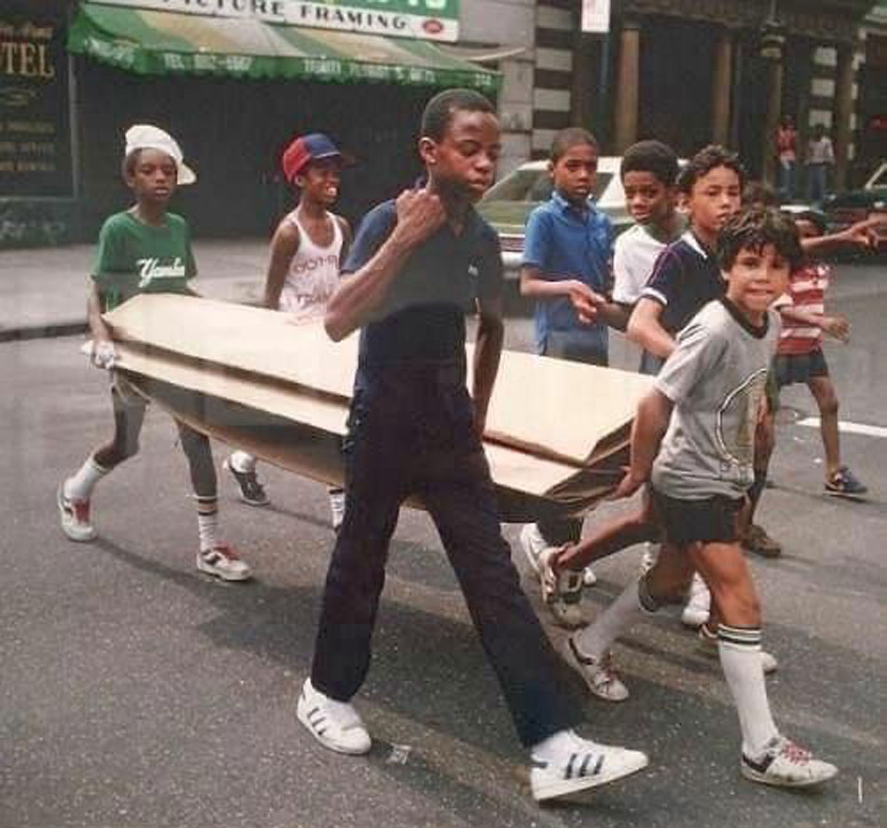 Group of kids carrying a large amount of cardboard across a street