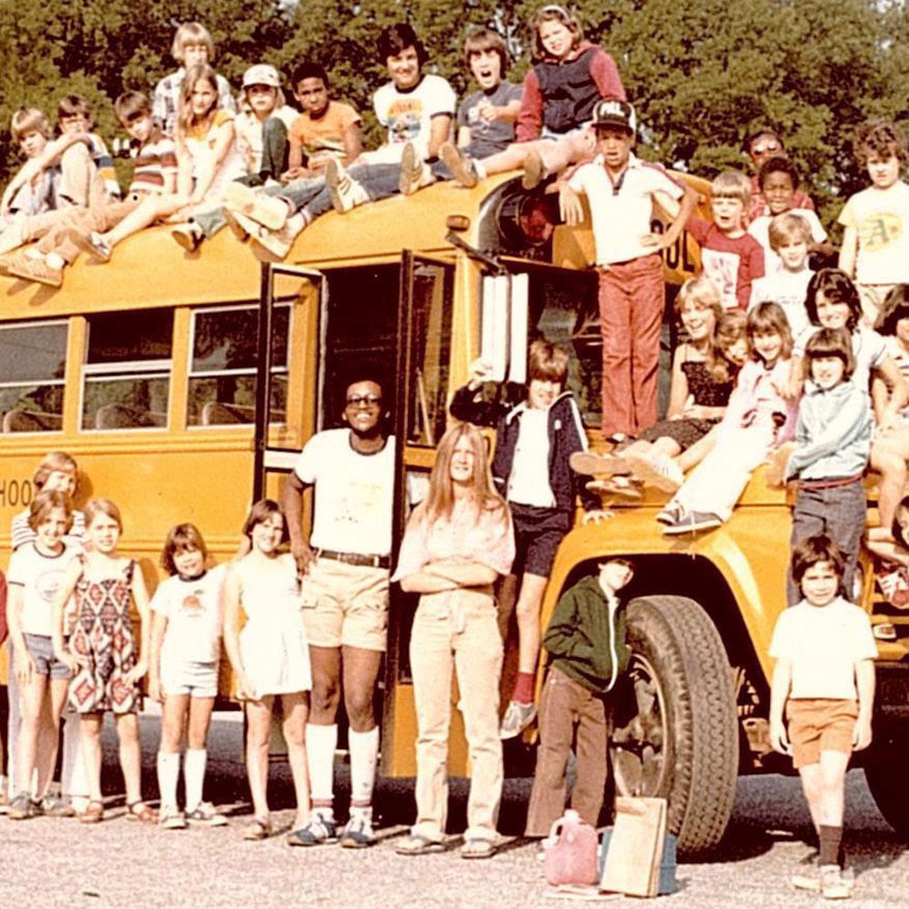 School bus driver in the middle of a photo of a school bus with kids all over and around it