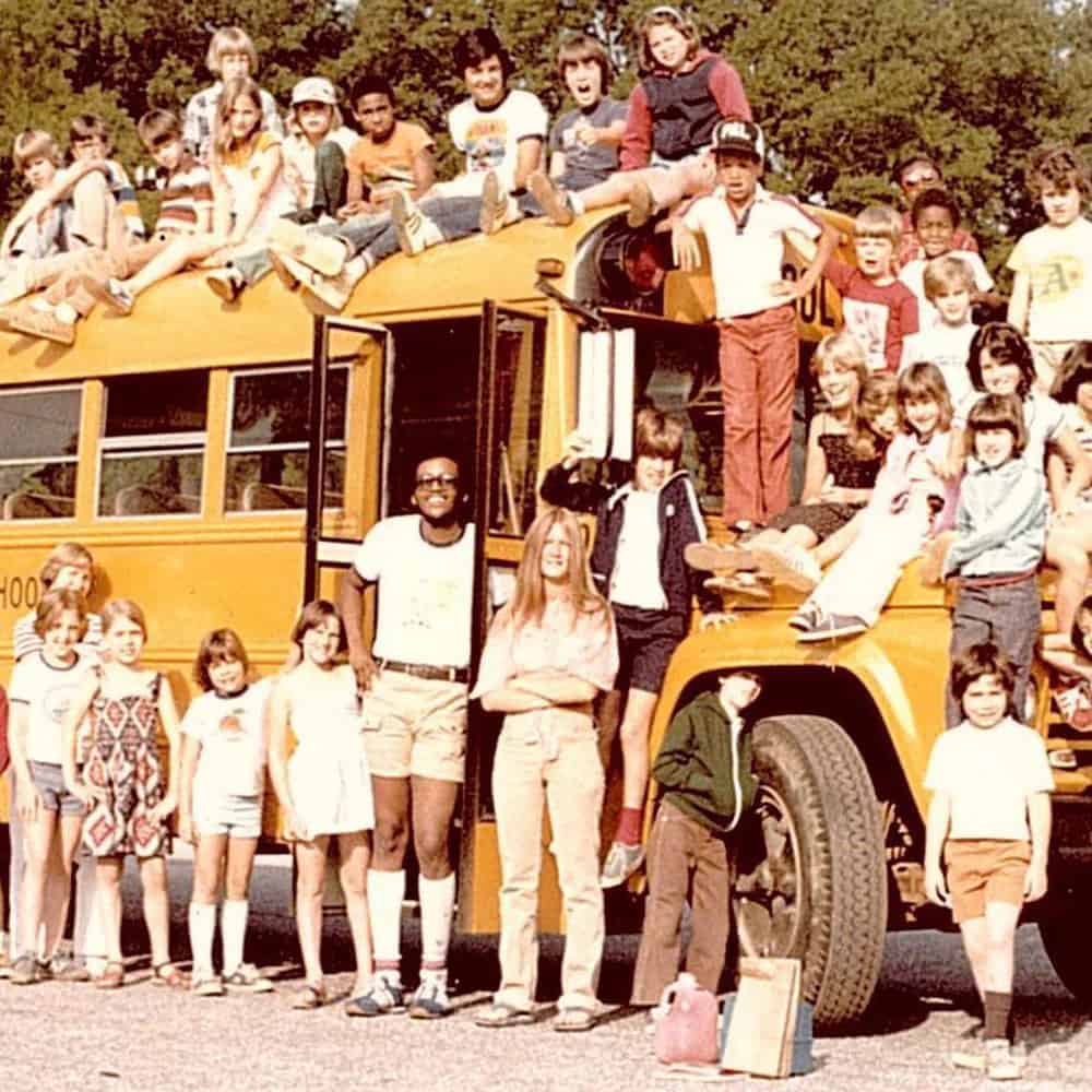 School bus driver in the middle of a photo of a school bus with kids all over and around it