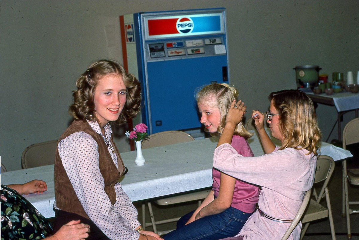 Three girls (and a fourth person mostly off-camera) sitting in a cafeteria