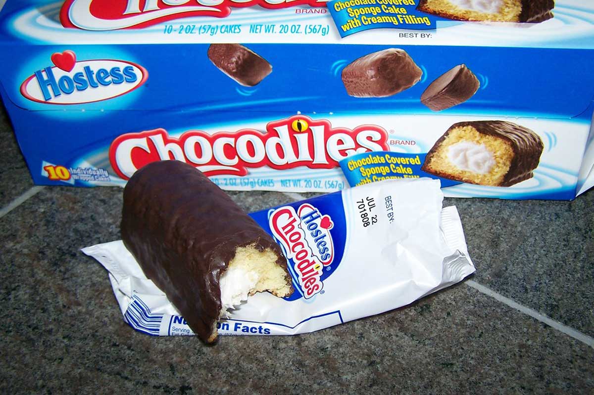 A half-eaten chocodile sitting on a wrapper in front of a box of Chocodiles