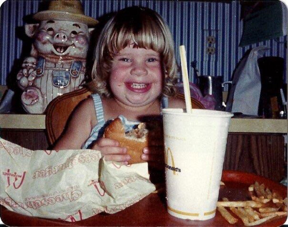 A kid with a huge smile on her face eating a McDonald's cheezburger