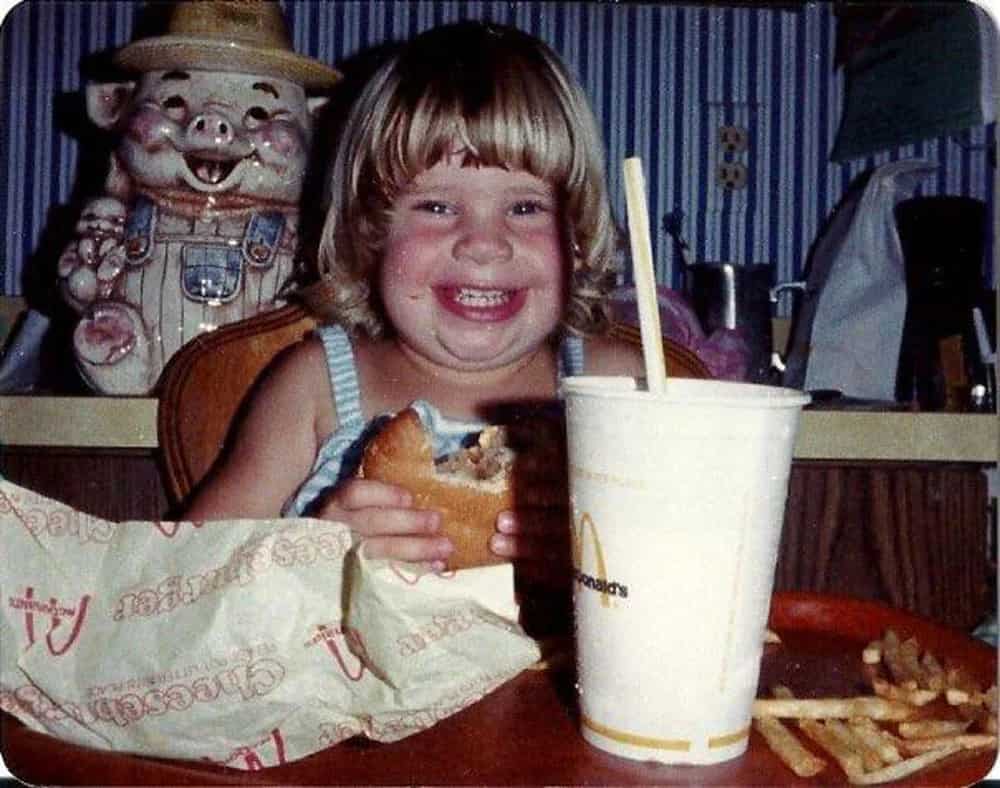 A kid with a huge smile on her face eating a McDonald's cheeseburger
