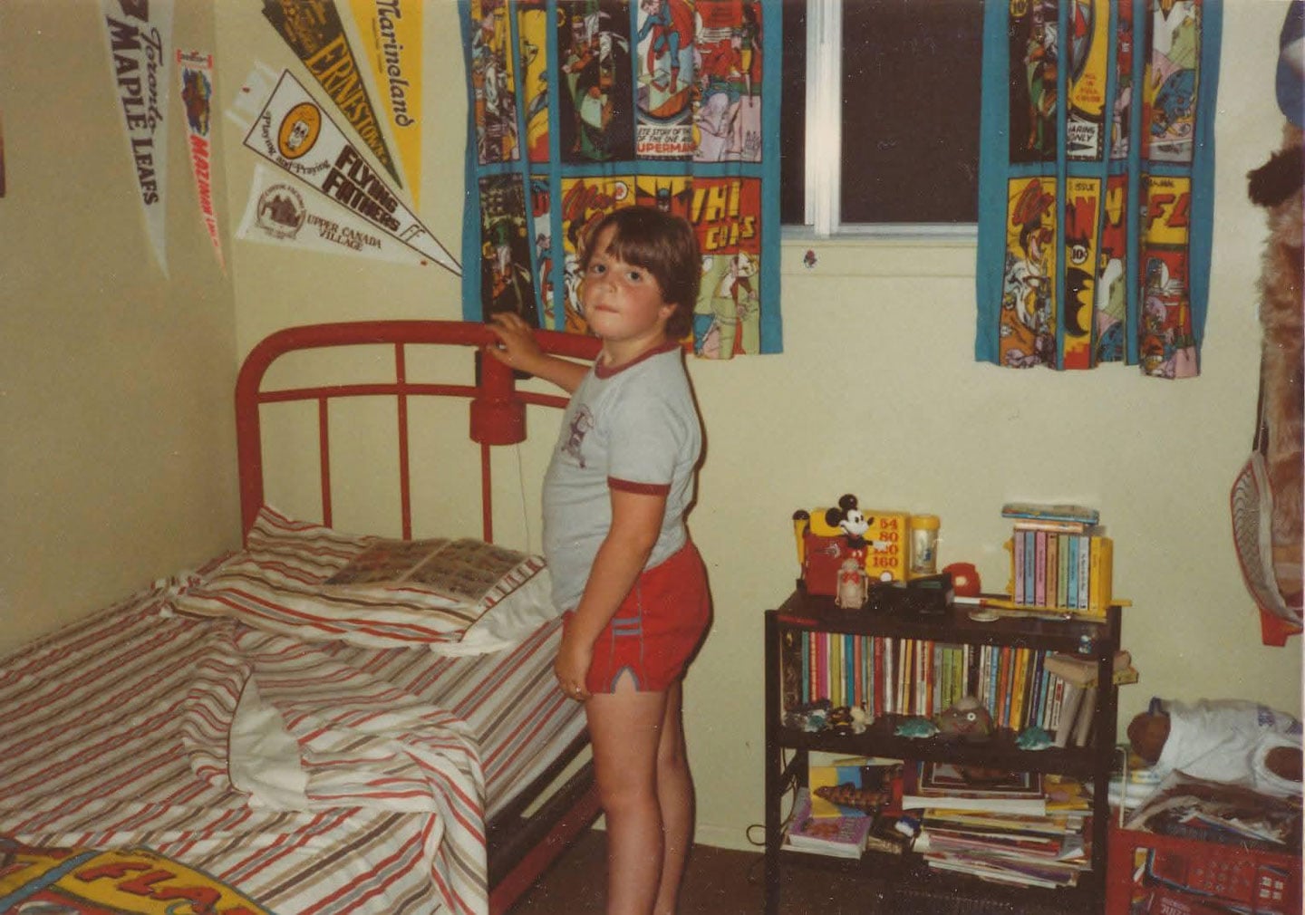 Boy in his room with sports pennants, comic book curtains, and lots of books