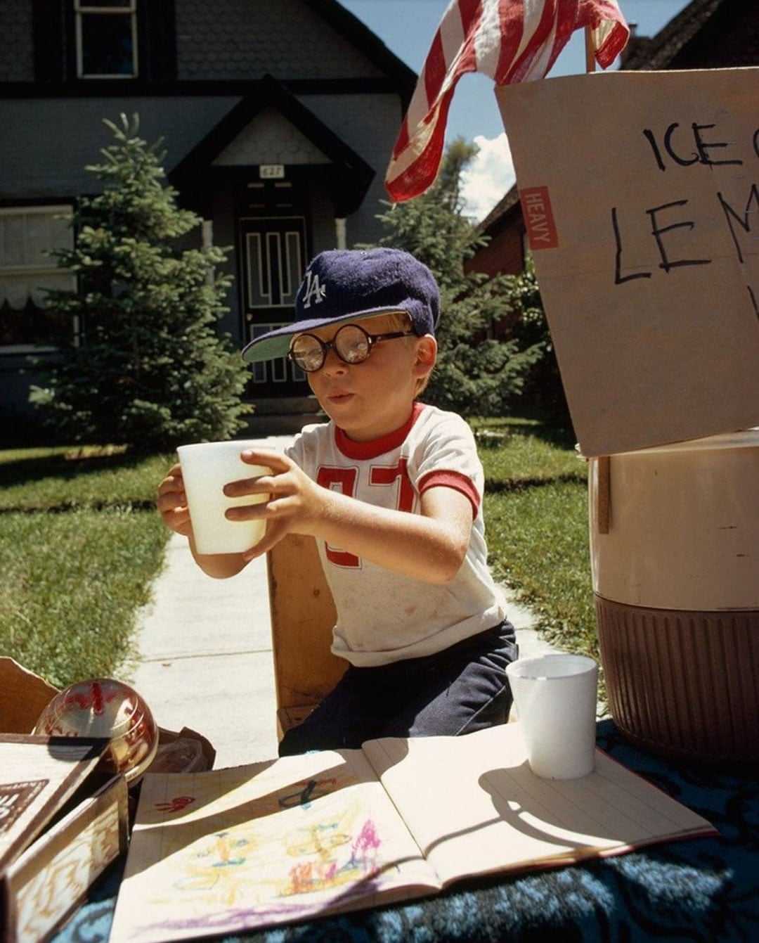 A boy wearing a Dodgers ball cap selling lemonade in his front yard