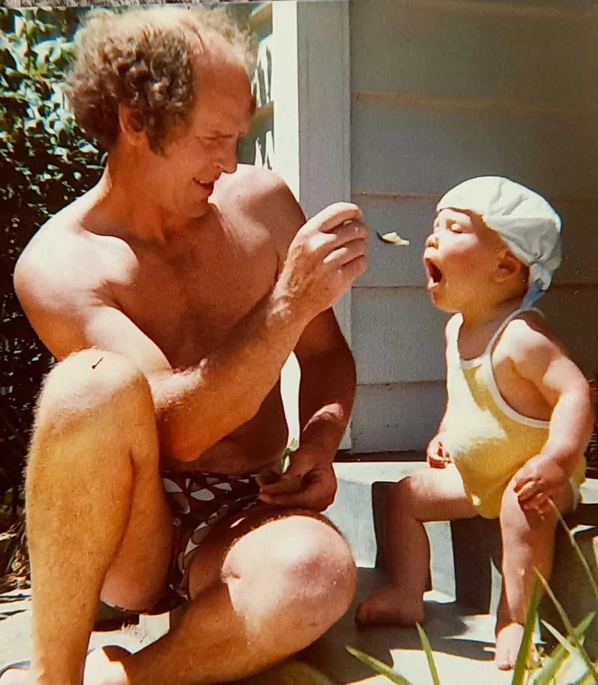 A father feeding his son on the porch on a sunny day.