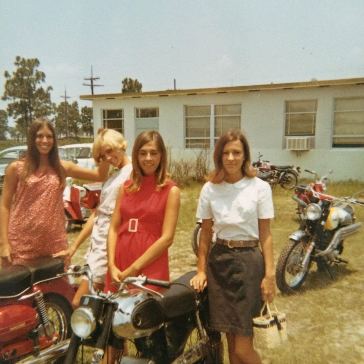 A group of young woman smiling and standing around their motorcycles