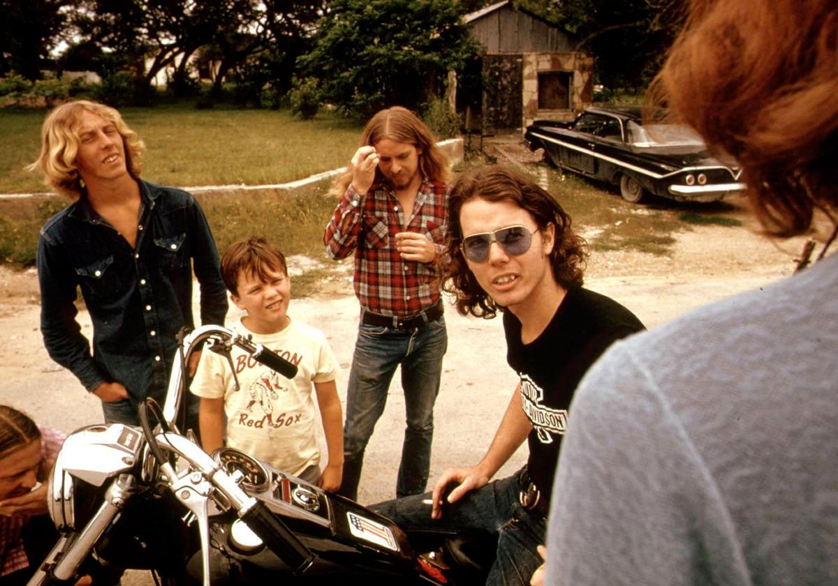 A man on the back on a motorcycle on the side of a road talking with some friends
