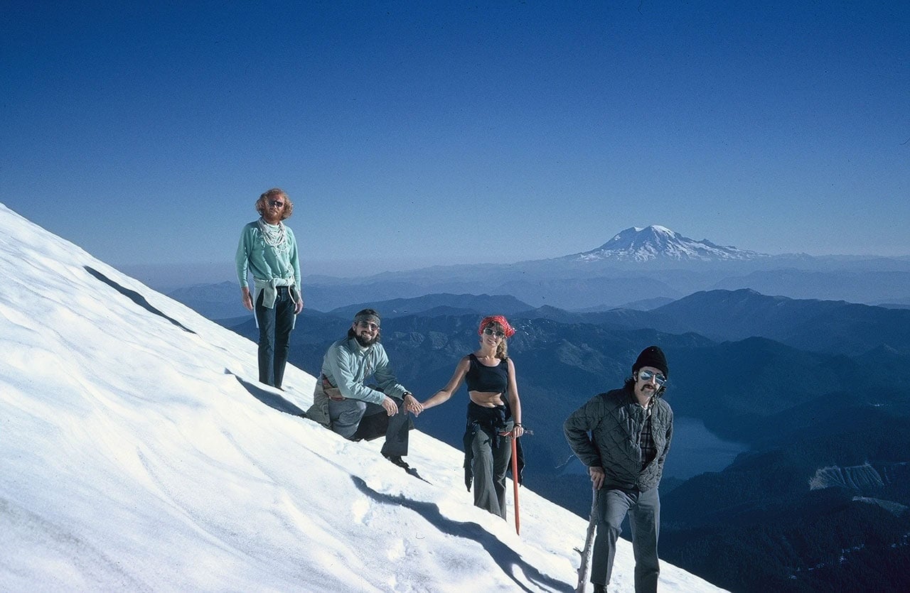Four people standing on a snowy mountainside with mountain in the distance