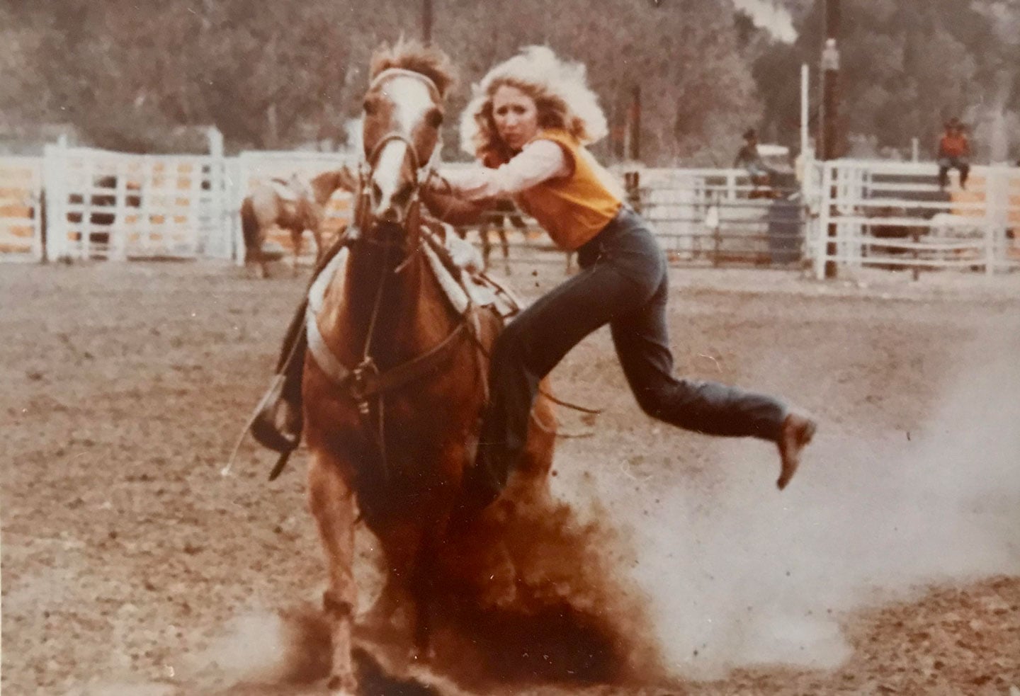 A woman riding a horse in a rodeo, kicking up dust