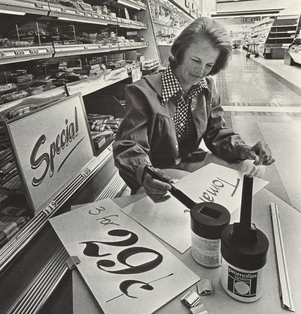 Woman sitting at a table in a grocery store painting the sale signs
