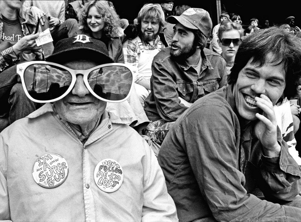 Black and white photo of fans at a Tigers game. An old man is wearing huge, funny sunglasses