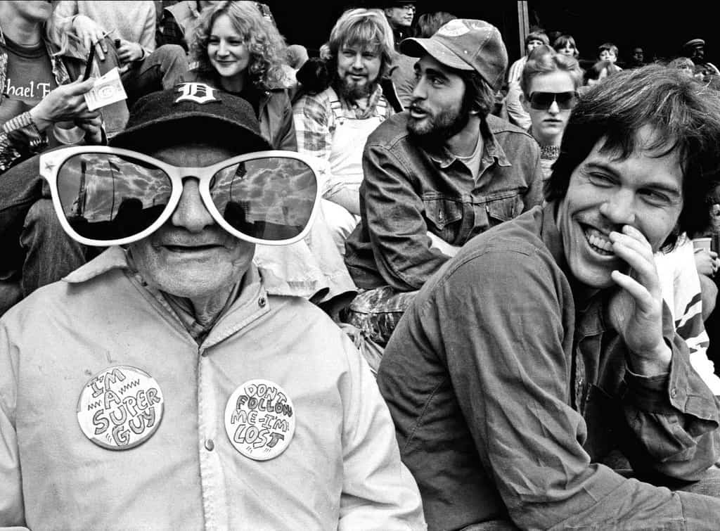 Black and white photo of fans at a Tigers game. An old man is wearing huge, funny sunglasses