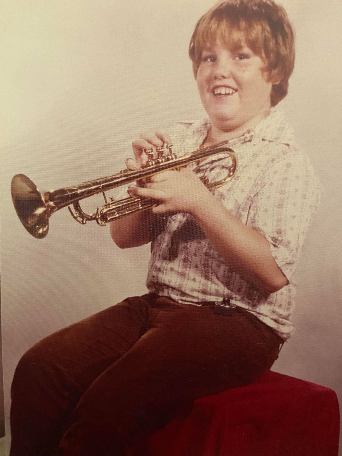 School photo of a kid holding a trumpet with a big smile on his face