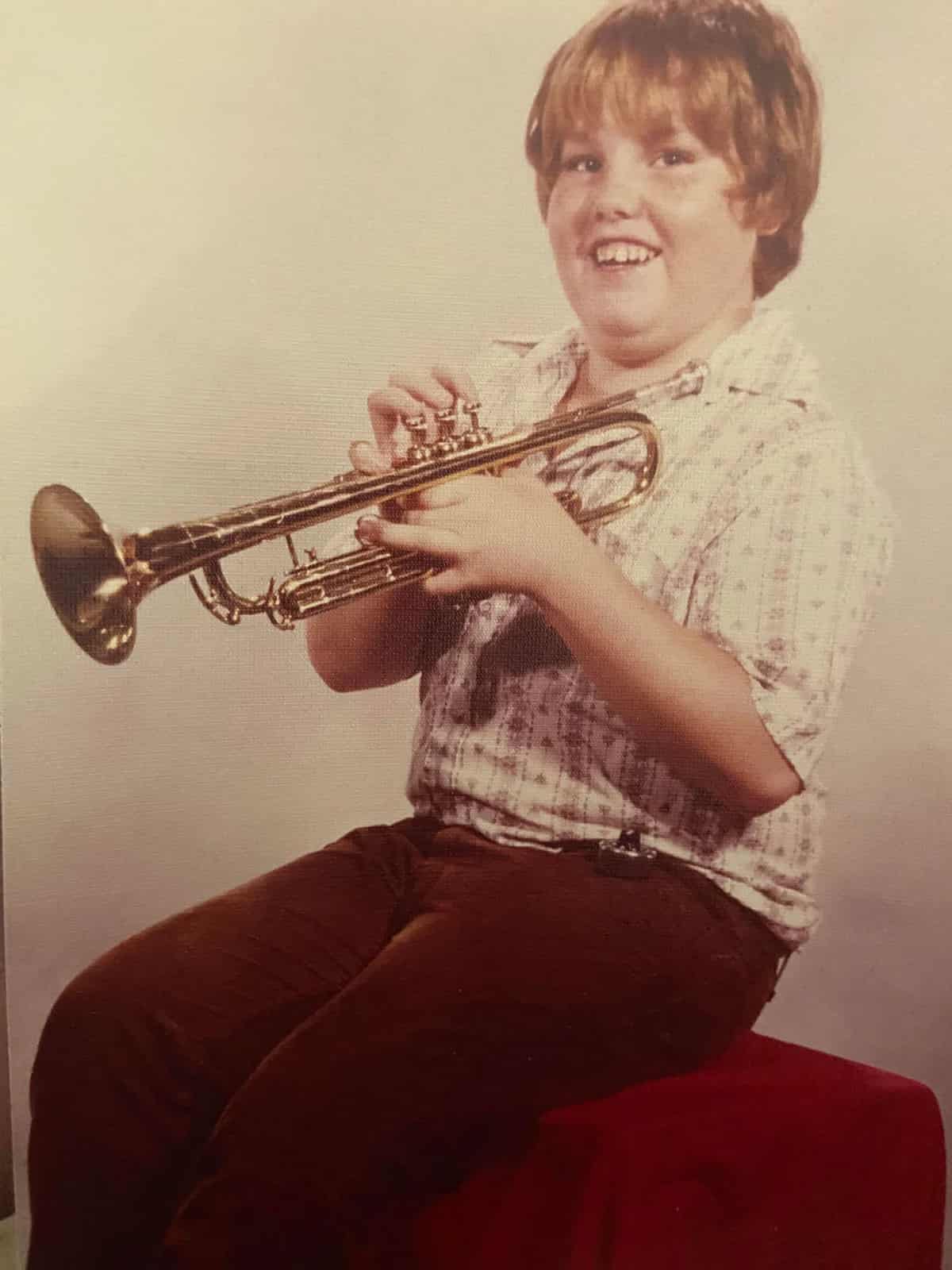 School photo of a kid holding a trumpet with a big smile on his face